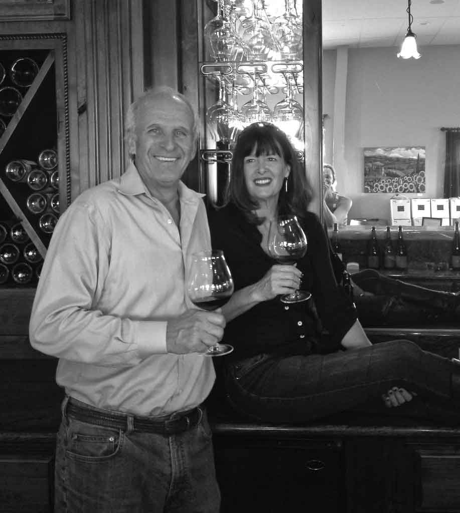 Our owners, Allen and Jill Methven, pose behind the bar at our tasting room, each holding a glass of wine.